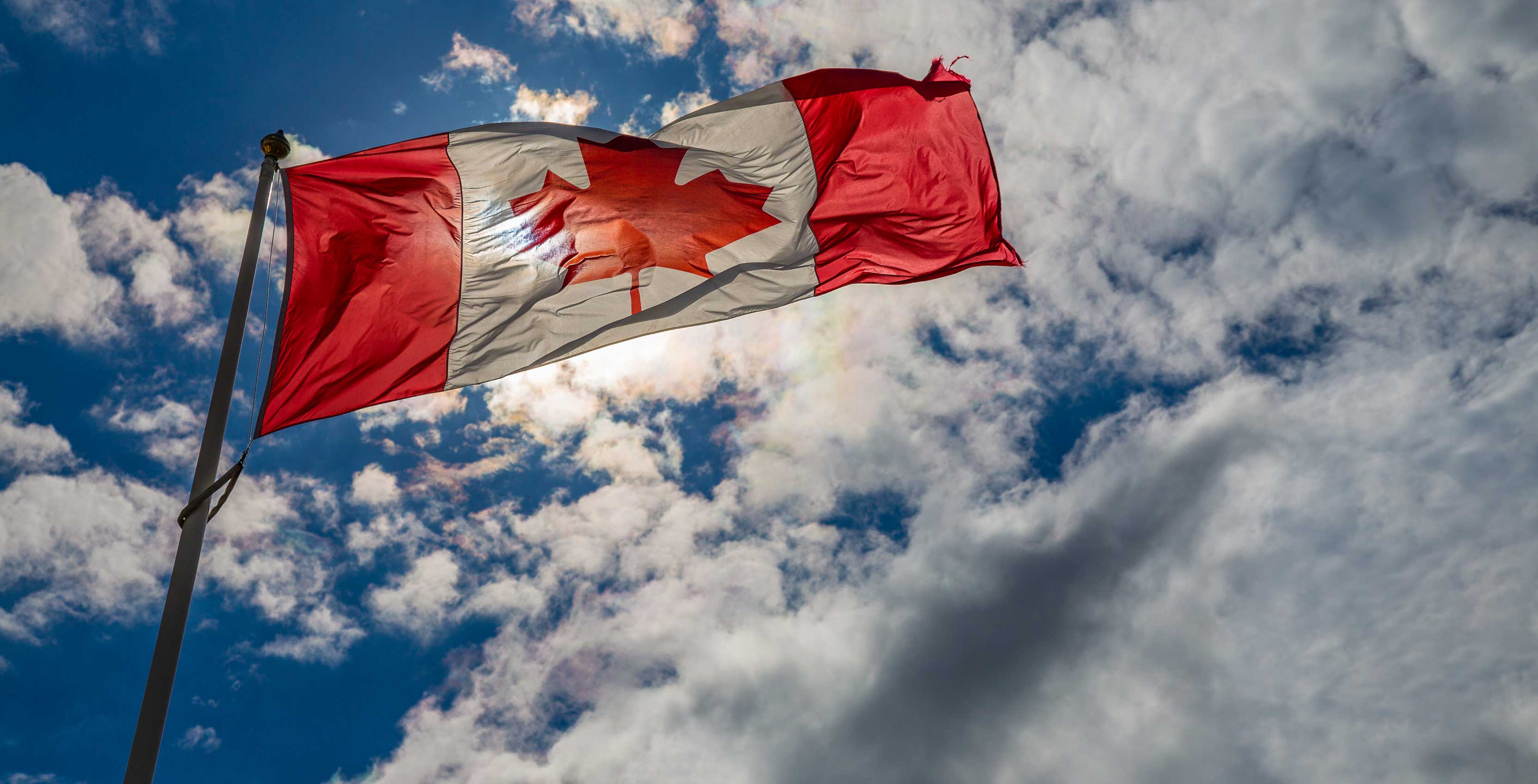 An image of the Canadian flag blowing in the wind against a backdrop of clouds