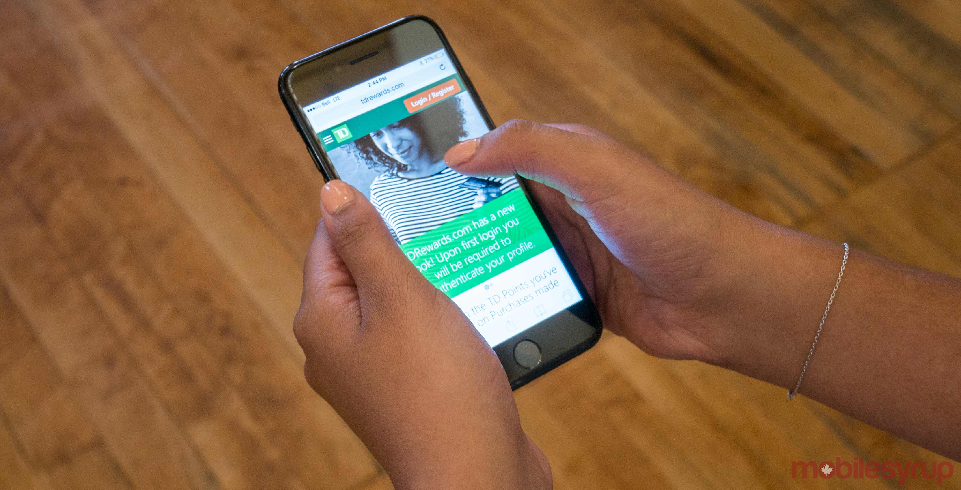 An image showing a hand holding an iPhone 7 with the TD Rewards website on-screen