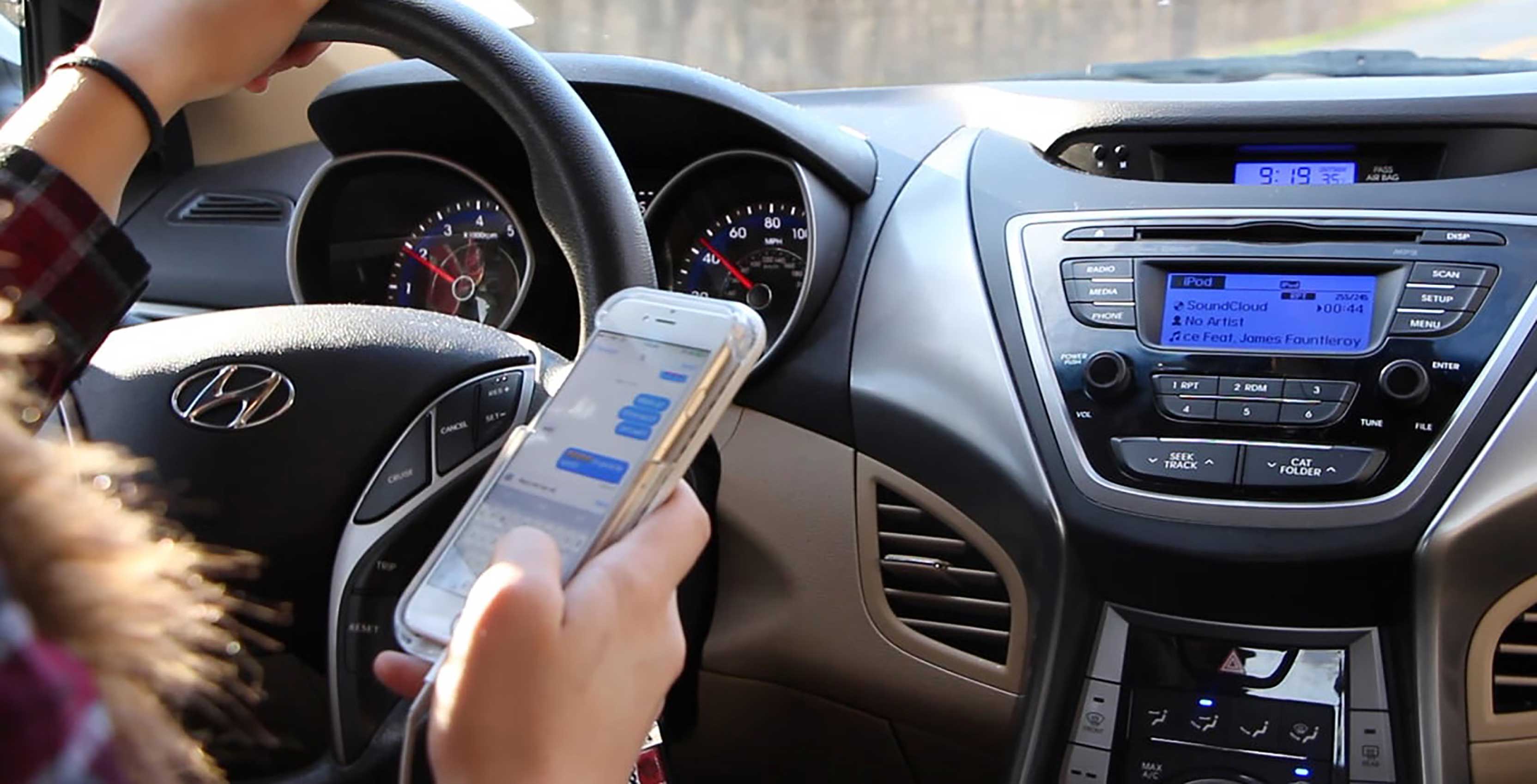 woman using phone behind steering wheel
