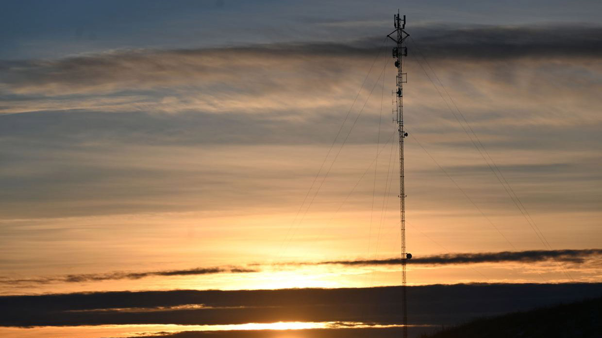 a cellphone tower in the distance in front of a sunset